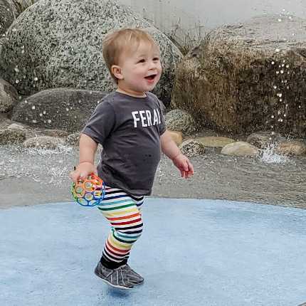 Funny Toddler T-Shirt worn by a joyful child playing outdoors with colorful striped pants.