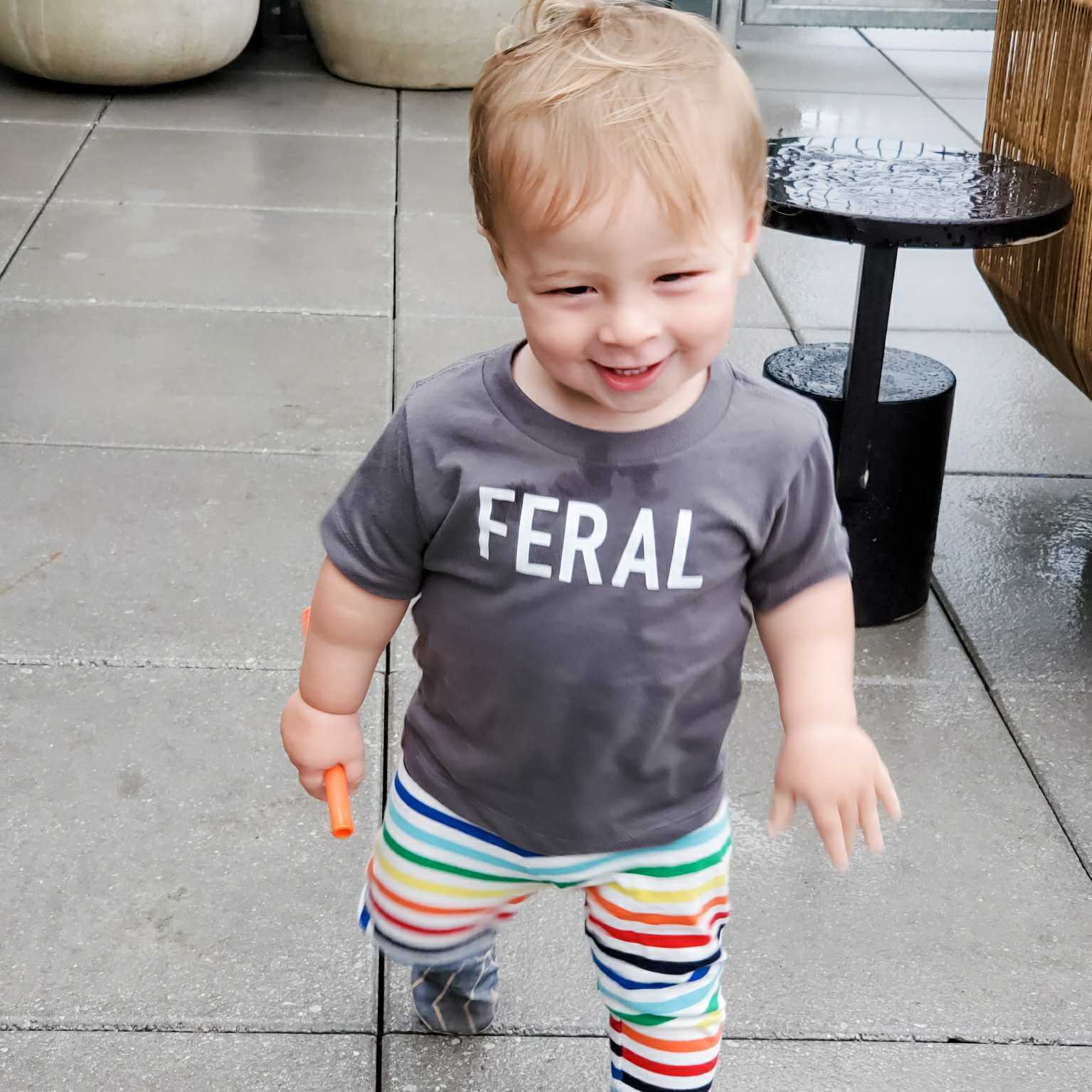 Funny Toddler T-Shirt: Happy child wearing FERAL t-shirt while playing outdoors, showcasing fun design and comfort.